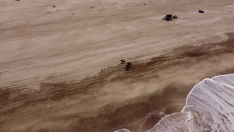 cinematic aerial shot showing group of people riding horses on sandy beach beside ocean during sunny day - mar de las pampas,argentina