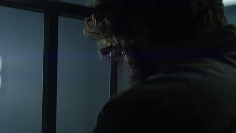 male criminal stands facing the metal bars in prison cell