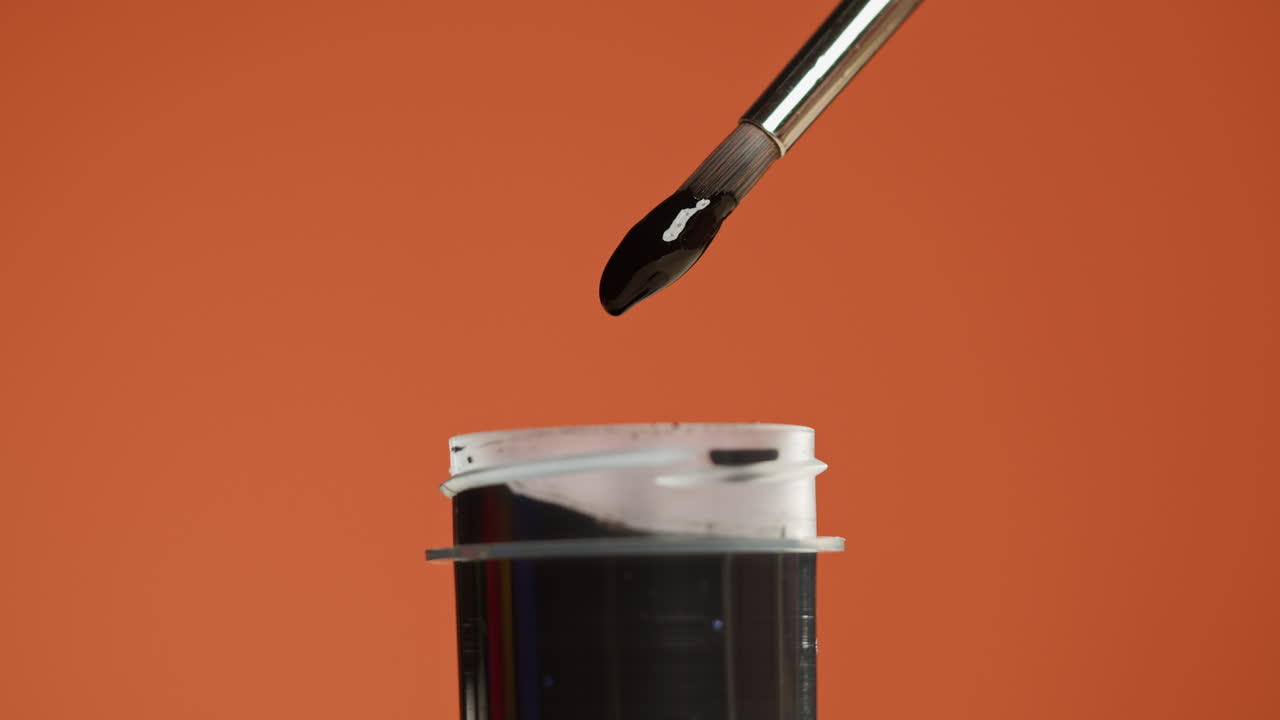Paintbrush Dipping into Black Paint on Orange Background