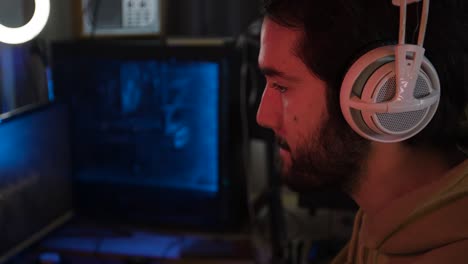 Male-gaming-on-a-pc-streaming-over-the-shoulder-white-headphones-blue-pc-in-background