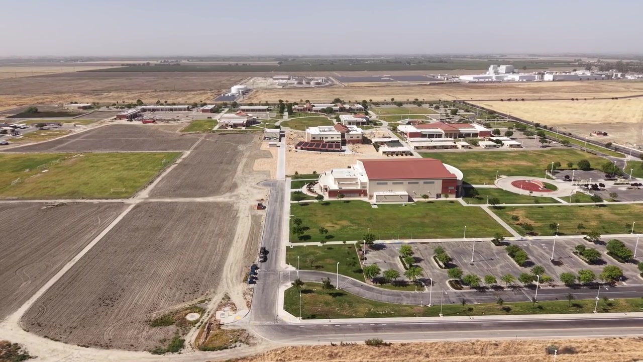 Vista in movimento da un drone che mostra il vasto campus del West Hills College a Lemoore, California, circondato da campi agricoli e un paesaggio rurale pianeggiante in una giornata limpida e soleggiata