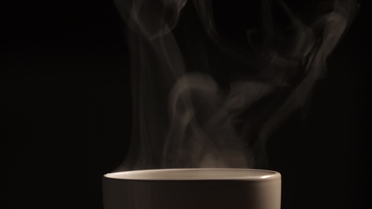 o chá quente ou café que está sendo derramado no copo branco tem fumaça branca e efeito de vapor no fundo preto