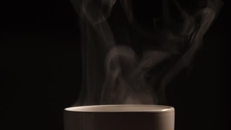 el té o café caliente que se vierte en la taza blanca tiene efecto de humo y vapor blanco en el fondo negro