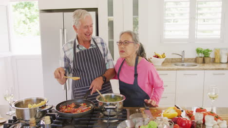 glückliches, vielfältiges älteres paar, das schürzen trägt und in der küche kocht