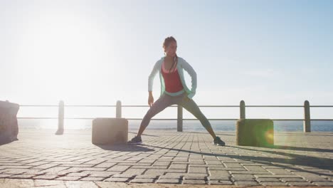 African-american-woman-in-sportswear-stretching-on-promenade-by-the-sea