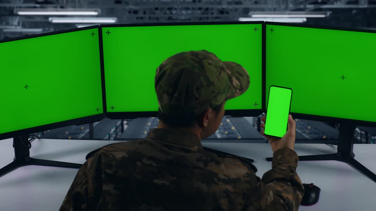 vista trasera del ejército asiático usando teléfono móvil y varios monitores de computadora con pantalla verde simulada en el centro de datos