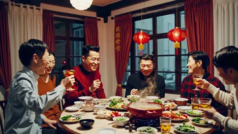 group of joyful asian male friends raising glasses for a toast, enjoying a traditional hot pot dinner together in a decorated room for lunar new year celebration