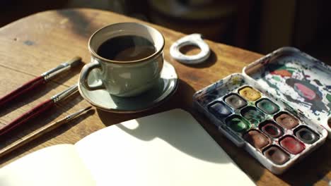a serene moment of creativity captured with a cup of coffee, an open sketchbook, watercolors, and paintbrushes, inviting artistic expression in a cozy workspace