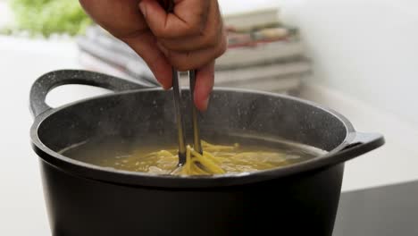 picking spaghetti from the boiling water in a pot, using a tong, in order to check their readiness