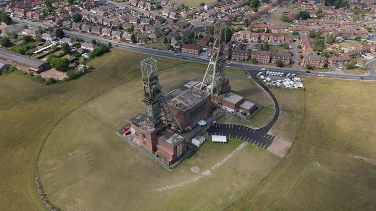 Ripresa aerea panoramica con drone orbitante di torri di miniera di carbone e strutture industriali storiche Clipstone Nottingham Inghilterra Regno Unito