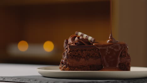 person pouring melted chocolate sauce on slice of chocolate cake before eating it with a fork