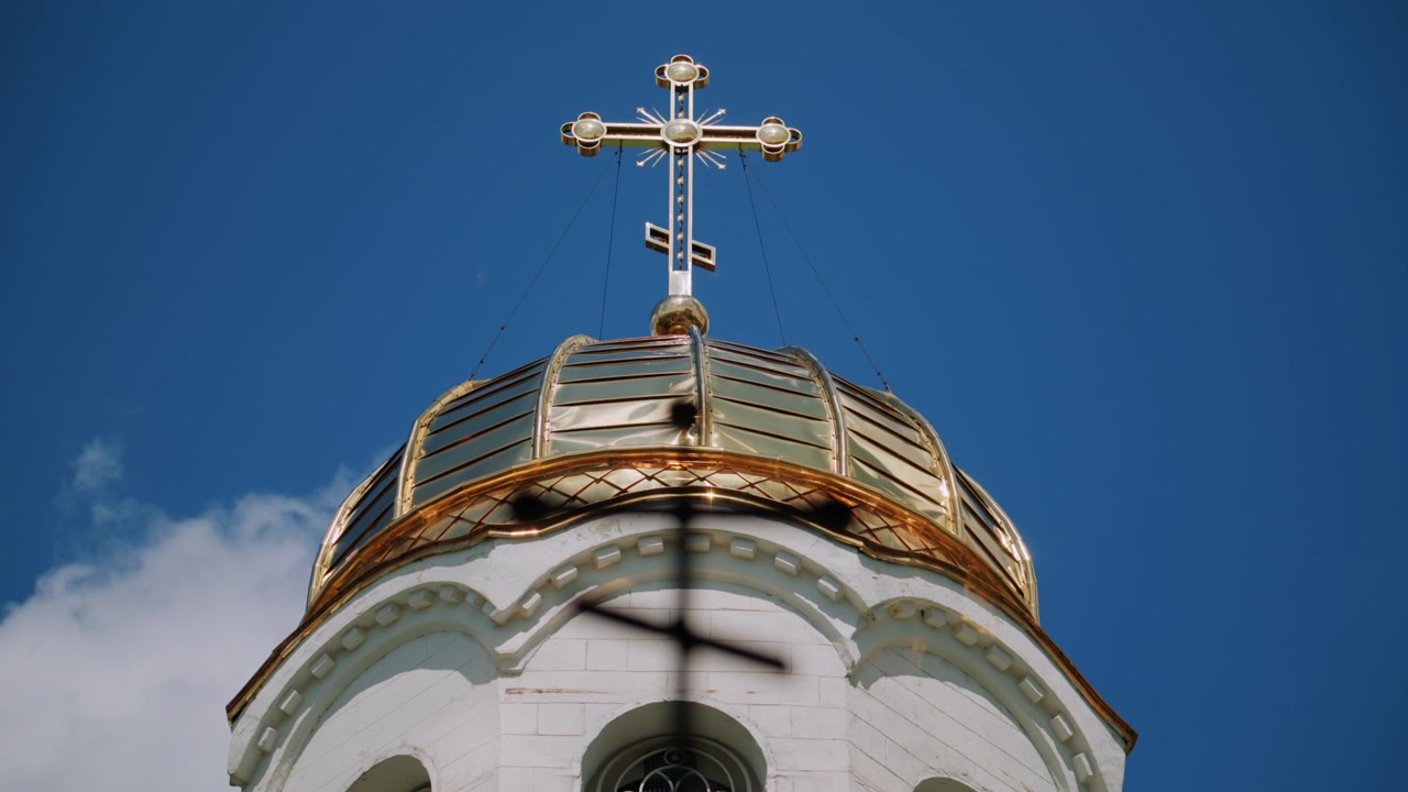 Foreground silhouette of a Christian cross with a softly blurred church dome and golden cross in the background