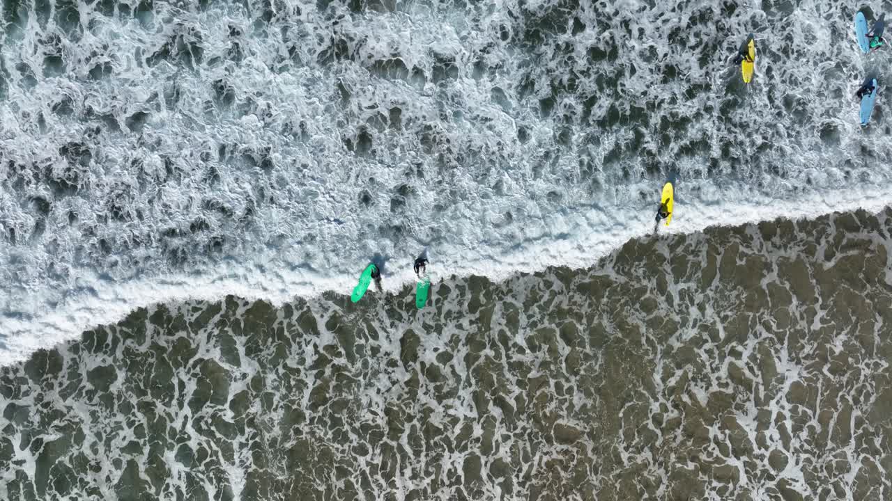 vista aérea de arriba hacia abajo de un surfista acabando con una ola espumosa que llega a la playa