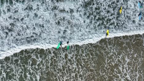 top-down aerial view of a surfer wiping out on a foaming wave rolling onto the beach