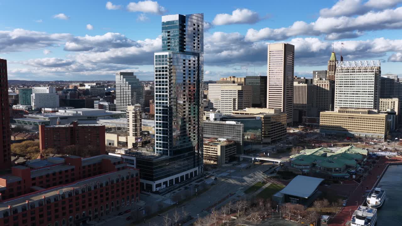 Luftfoto af Baltimores centrum med Inner Harbor-vandfronten, moderne skyskrabere, historiske bygninger og både langs havnen under en lys himmel. Livlig urban bysilhuet af en amerikansk storby