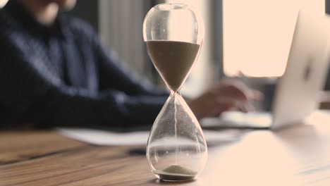 businesswoman working on laptop focus on hourglass showing time passage