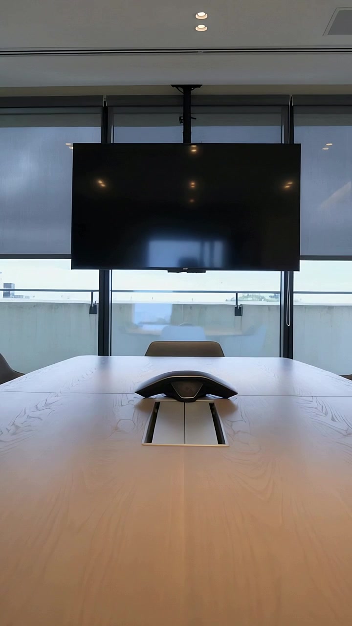 縦型動画：電話と壁掛けテレビがあるオフィスで、移り変わる雲が長いテーブルに光を映し出す様子。