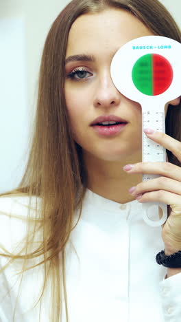 young woman checking eyesight. pretty girl doing vision test with one eye closed by occluder. ophthalmology. vision check-up. vertical video