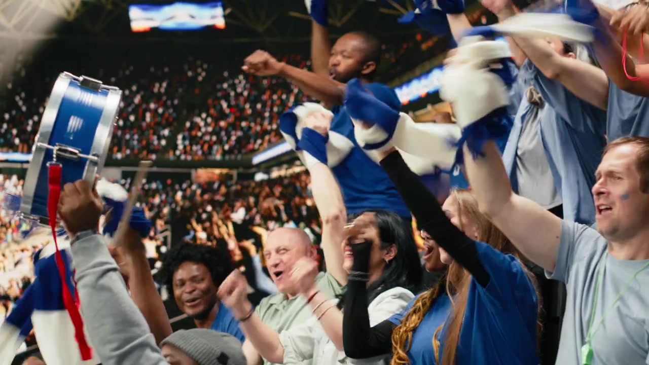 Diversos aficionados de fútbol azules levantando los brazos y coreando juntos.