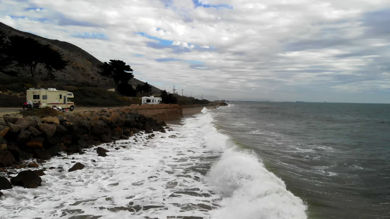 흐린 날 공중 드론이 태평양 파도 위로 낮게 웅크리고 캘리포니아 rv 캠핑카 옆에 있는 바위가 많은 벤투라 해안에 충돌했습니다.