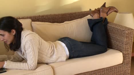 brunette woman lying down on sofa using a laptop