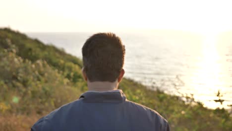 traveler wearing jacket walking on a mountain top approaching the ocean.