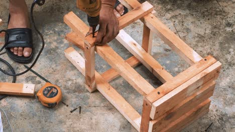 skillfull carpenter employing a power drill to attaching screws into a small wooden chair in his small business workshop to sell and support the local economy