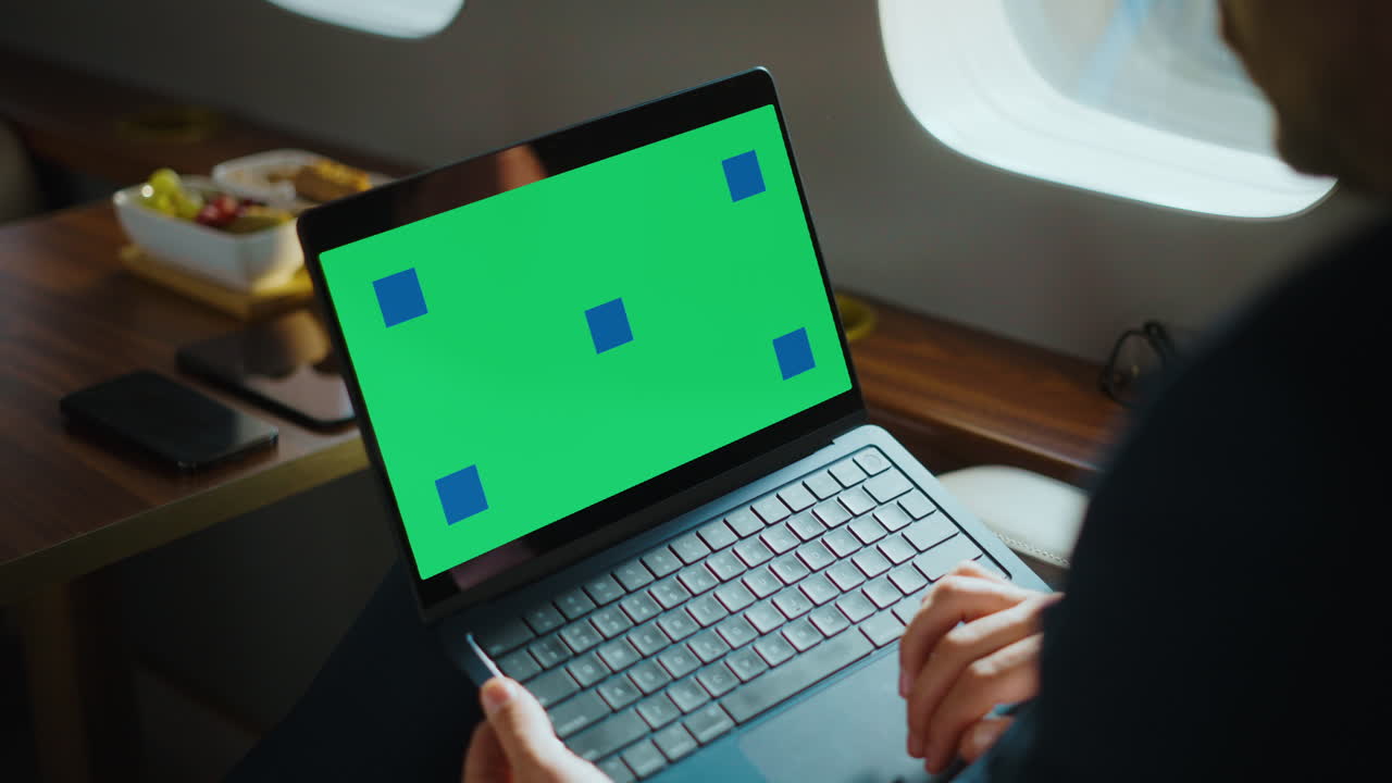 Man using laptop with green screen on private jet
