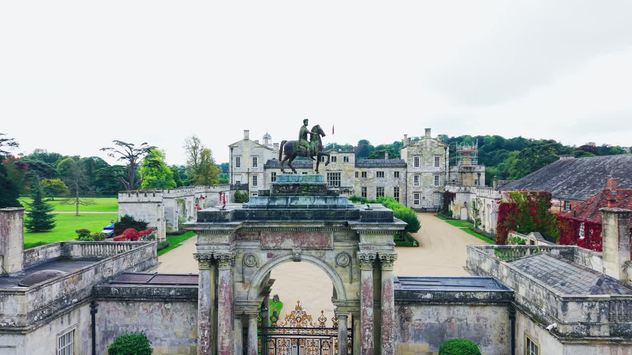 Luchtopname met drone die de historische ingangsboog en het grote landgoed Wilton House in Wiltshire, Engeland, nadert, met klassieke Britse landhuisarchitectuur en terreinen