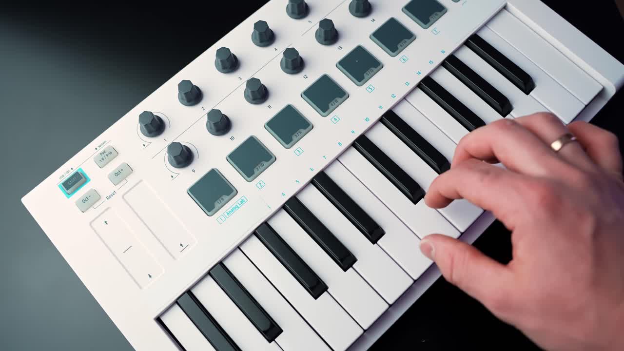 Primo piano di una mano che suona una melodia su una tastiera controller MIDI compatta con pad e manopole su una scrivania, che mostra un moderno flusso di lavoro per la registrazione domestica e la produzione musicale.