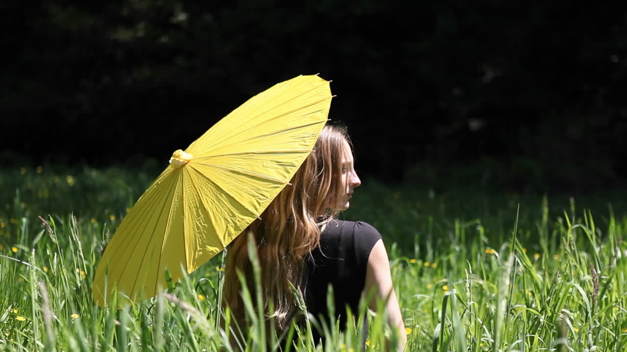 한 여자가 우산을 들고 높은 잔디밭에 앉아 있다