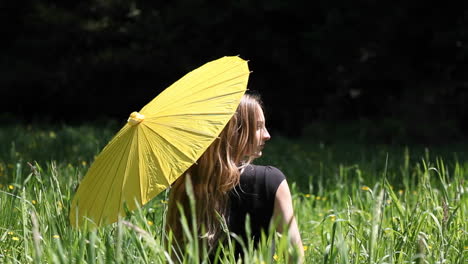 a woman sits in a tall grassy field with an umbrella