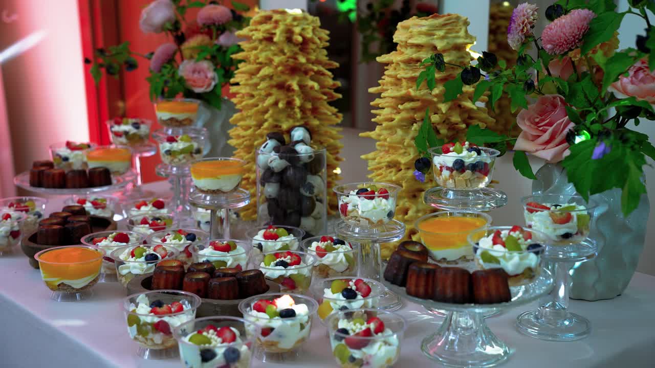 Et smukt arrangeret dessertbord med forskellige søde sager, kager og blomsterdekoration under varm belysning, hvilket skaber en indbydende og elegant atmosfære. Perfekt til arrangementer