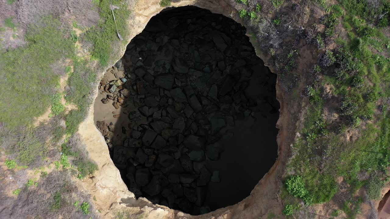 Mesmerizing drone shot captures the unique view of a circular hole carved into the cliffs at the beach as the drone slowly ascends, revealing the stunning natural formations that surround it