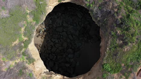 la fascinante toma de un dron captura la vista única de un agujero circular tallado en los acantilados de la playa mientras el dron asciende lentamente, revelando las impresionantes formaciones naturales que lo rodean.