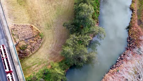A red semi-truck drives across a rural bridge above a river, viewed from directly overhead. Morning light, drone footage, visible exhaust trail