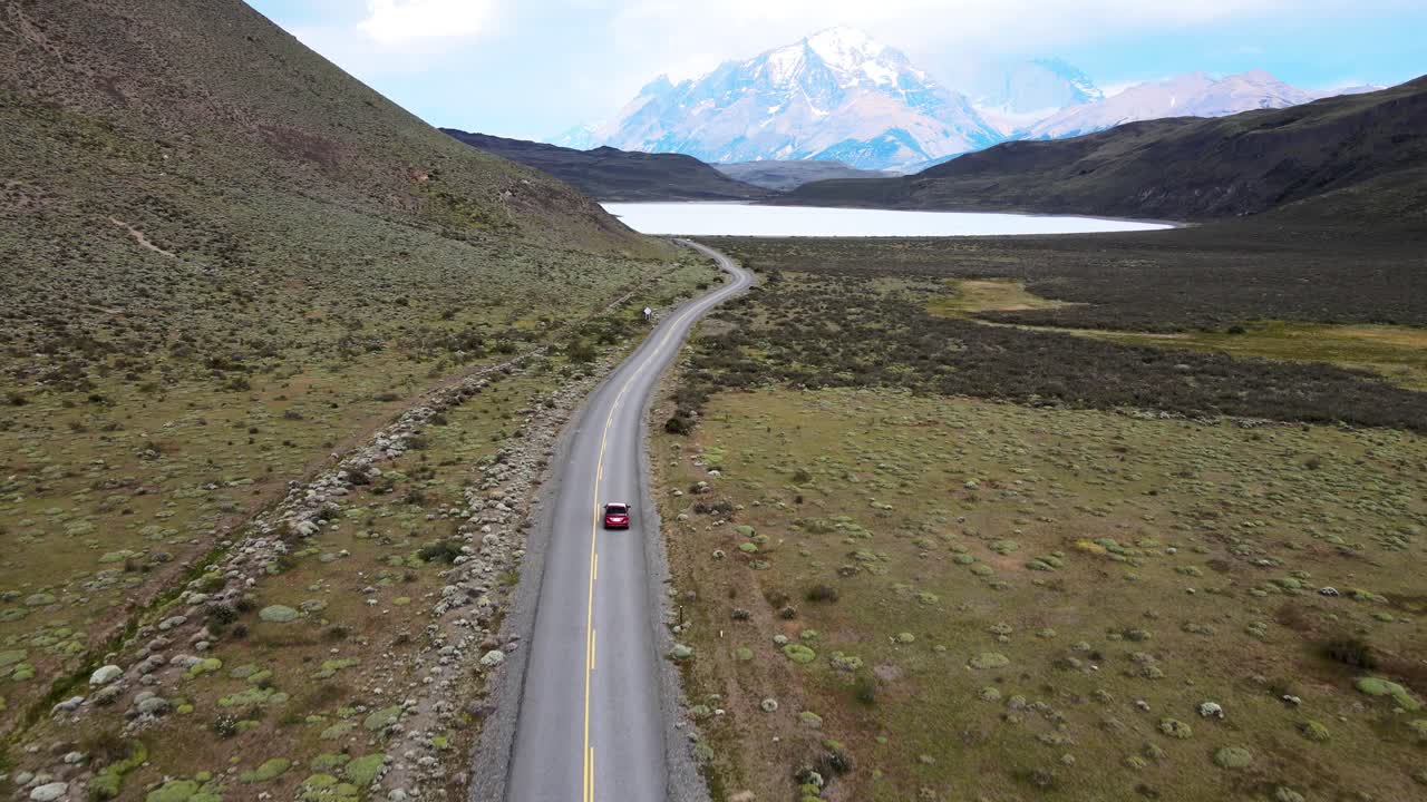 Volo fluido di drone in Patagonia con un'auto su una lunga strada che porta alle montagne.