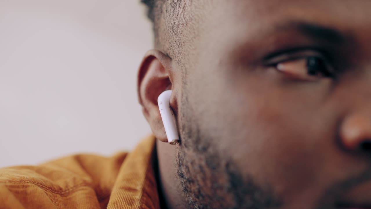 African American man putting wireless earbuds in his ears, enjoying new device