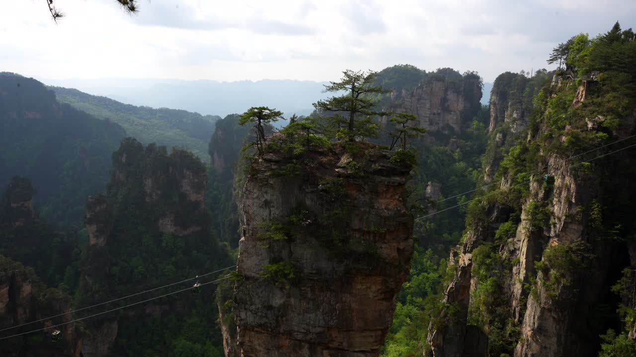 Cable cars move behind a towering sandstone pillar in Huangshi Village, China. Static establishing shot