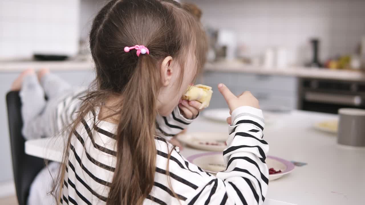 dos hermanas pequeñas comen panqueques en la mesa con el padre detrás de ellas. vista lateral