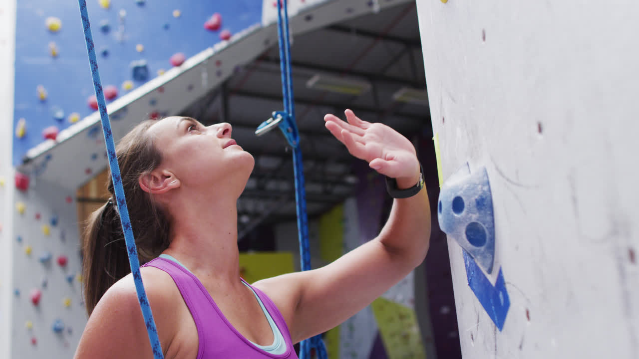 mujer caucásica nerviosa preparándose para escalar una pared en una pared de escalada interior