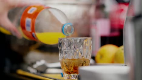 orange soda being poured into a crystal glass with fruit blurred in the background
