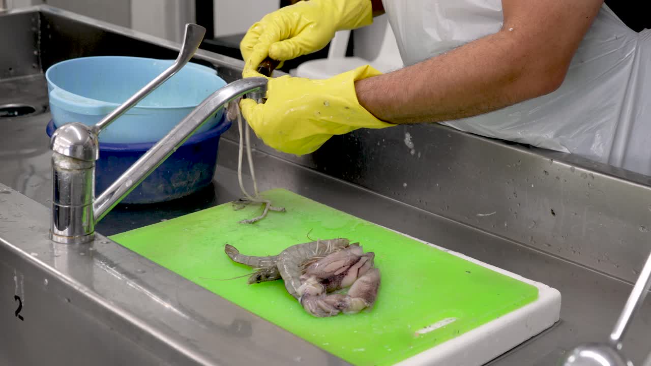 In a lively kitchen, a skilled chef cleans and prepares fresh shrimp with expert technique. Bright green cutting boards and shiny utensils create an inviting atmosphere