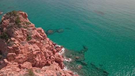 bird eyes view over a red cliff with tropical water sea on the beautiful sunny day in sardinia, italy - aerial drone shot