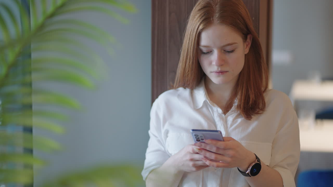 Smiling businesswoman using phone in office. Small business entrepreneur looking at her mobile phone and smiling. Woman texting in modern office