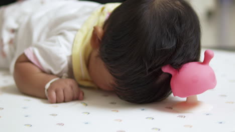 Baby girl practicing the skill of rolling over on the bed with developmental toys. A moment of early learning and growth in infant motor skills, captured with playful and colorful toys.