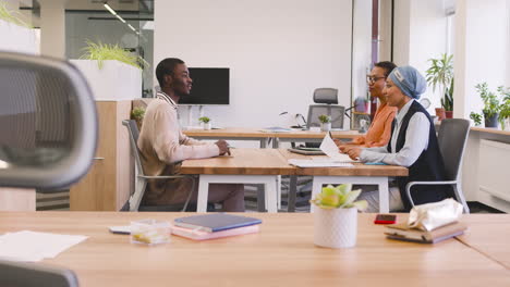 an woman and a muslim woman co workers interview a young man sitting at a table in the office 14