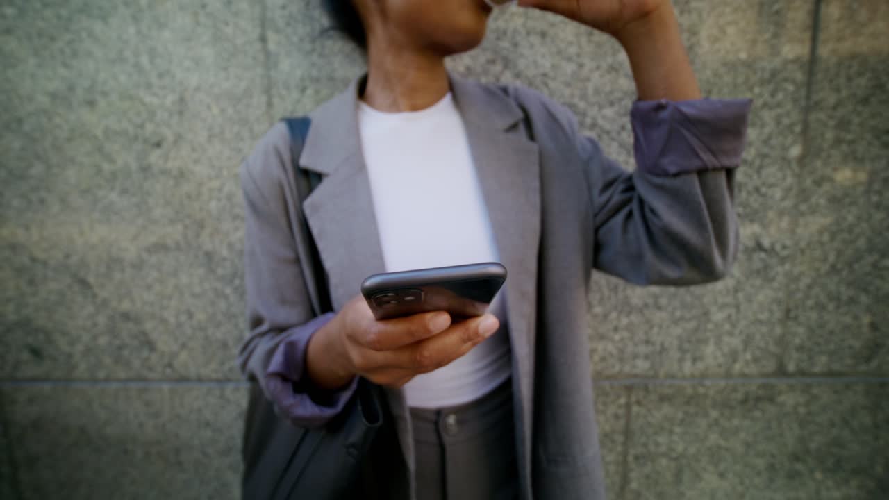 여성이 드폰을 사용하고 야외에서 커피를 마시고 있습니다.