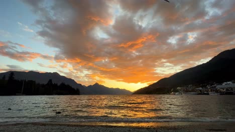 glowing orange sunset over lake wakatipu, new zealand with seabirds crossing frame