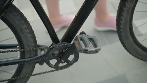 close-up of person in pink sneakers strolling with bicycle along paved path, capturing bicycle pedal, chain, and back tire detail, conveying outdoor movement and relaxed summer vibe in urban setting